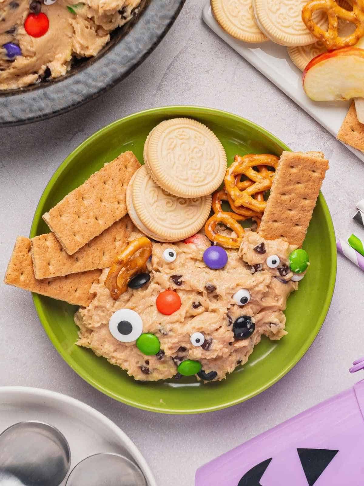 Edible cookie dough on a green plate with cookies and pretzels.