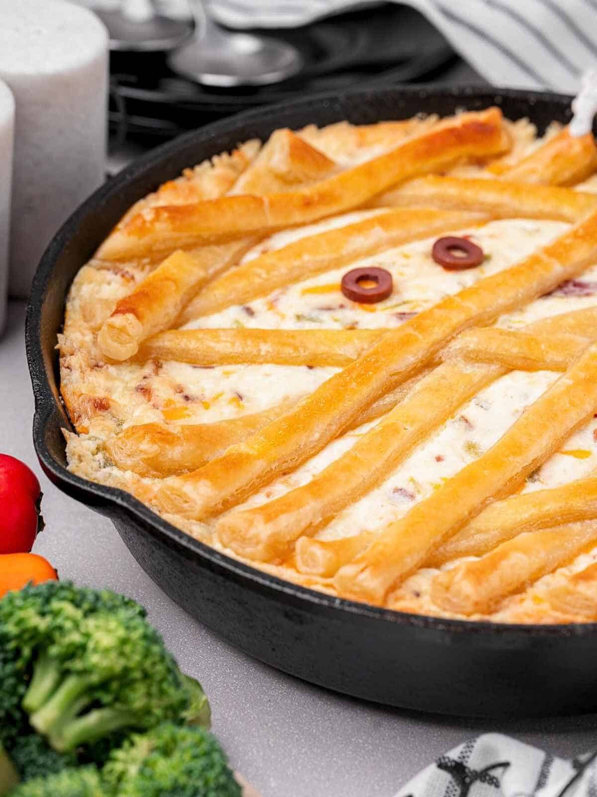 Black cast iron skillet with puff pastry bandages and olive eyes.