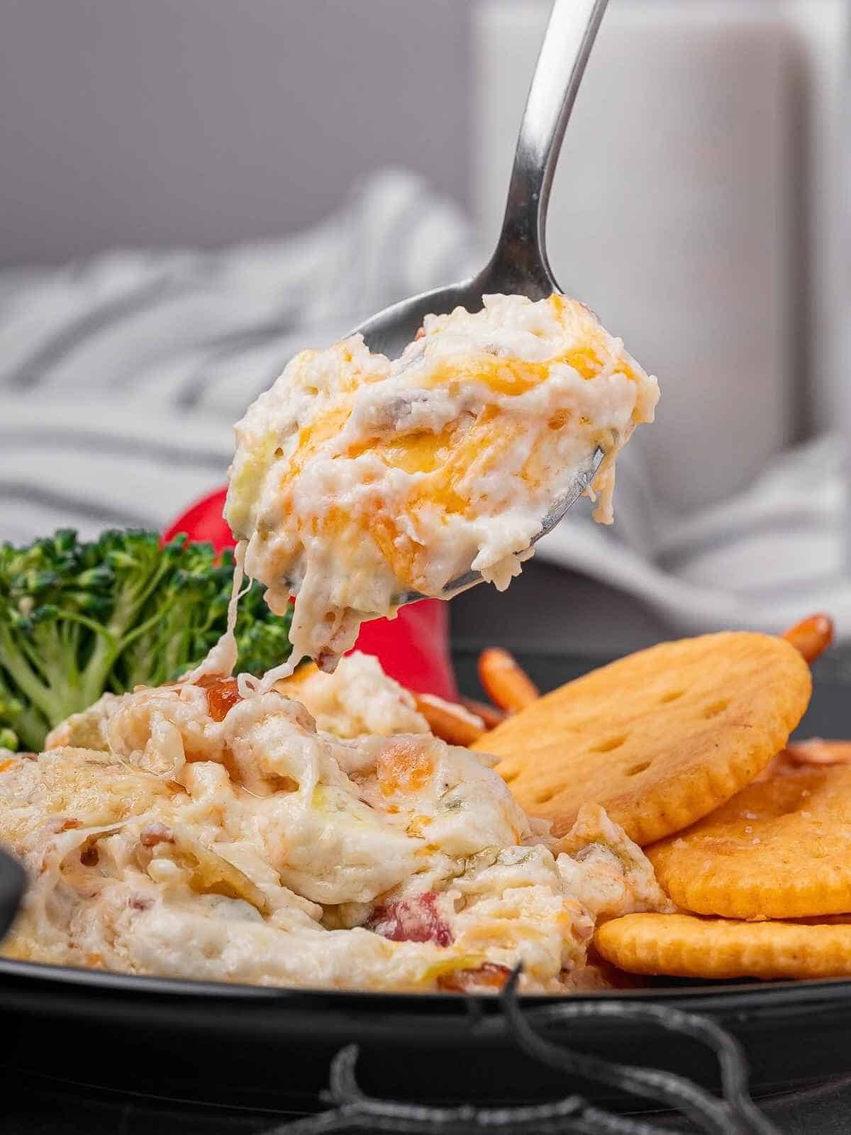 Spoonful of jalapeño popper dip being lifted up over a black plate.