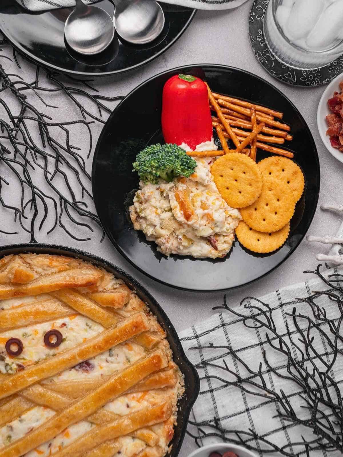 A black plate of jalapeno popper dip with veggies on a spooky tablescape.