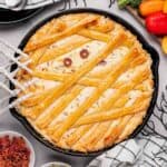 Jalapeno popper dip with mummy bandages and olive eyes in a cast iron skillet.